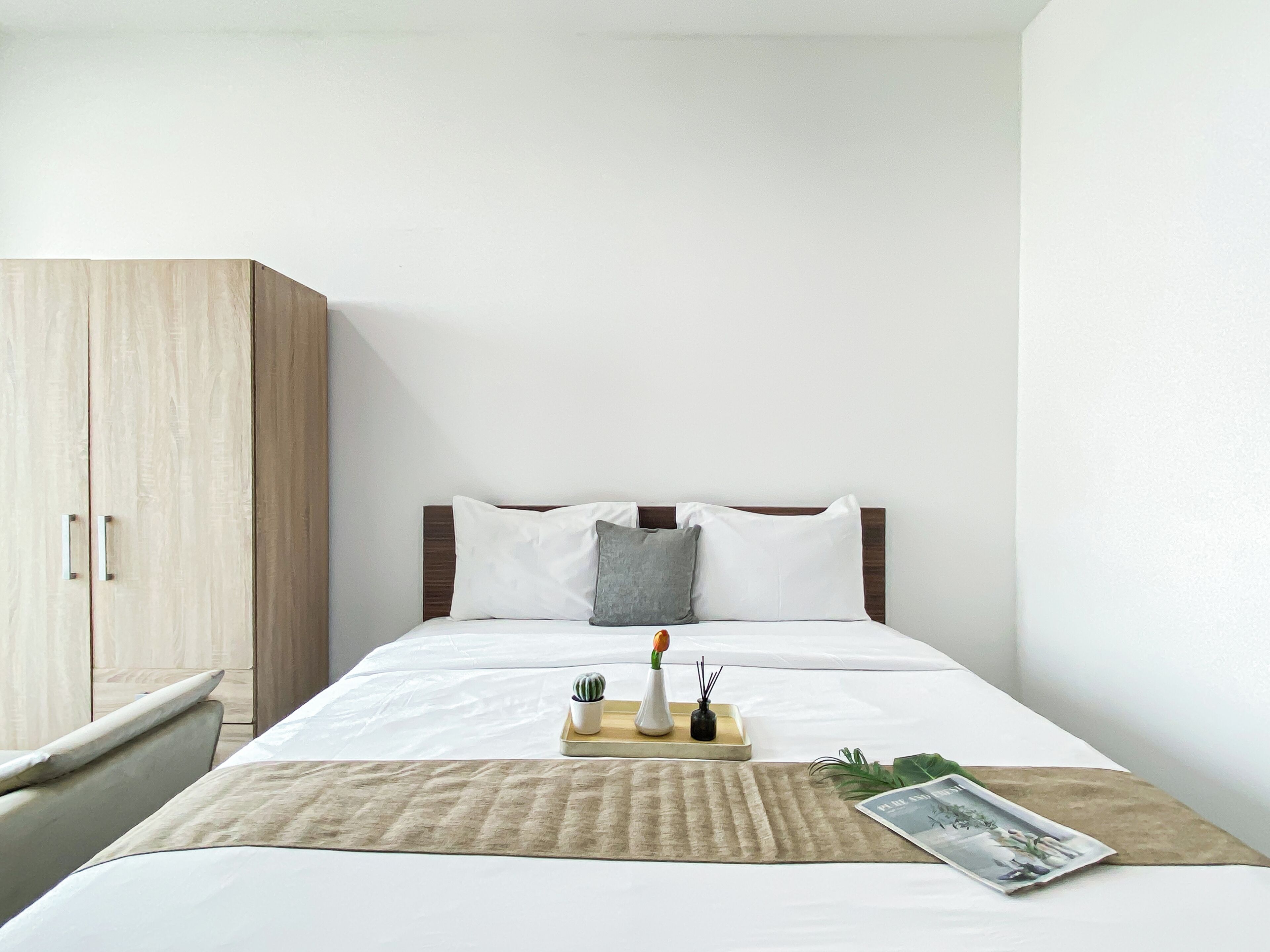 A hotel room with a bed, a wooden wardrobe, a bedside table, and a tray with a plant and a candle.