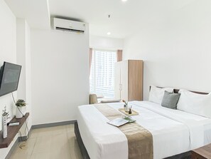 A hotel room with a bed, a TV, an air conditioner, and a window with curtains.