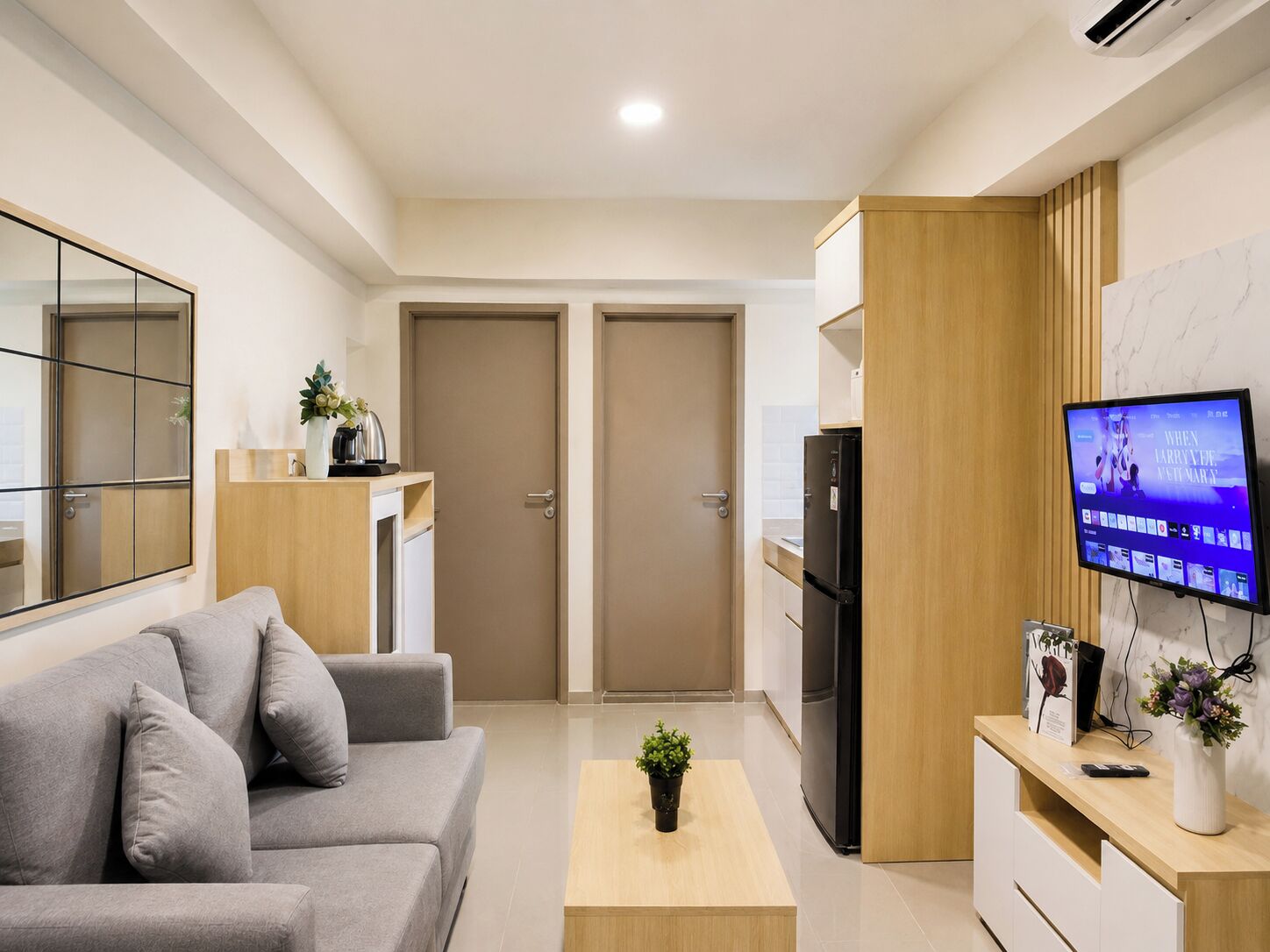 Una sala moderna con un sofá gris, una mesa de centro de madera y un televisor montado en la pared.
