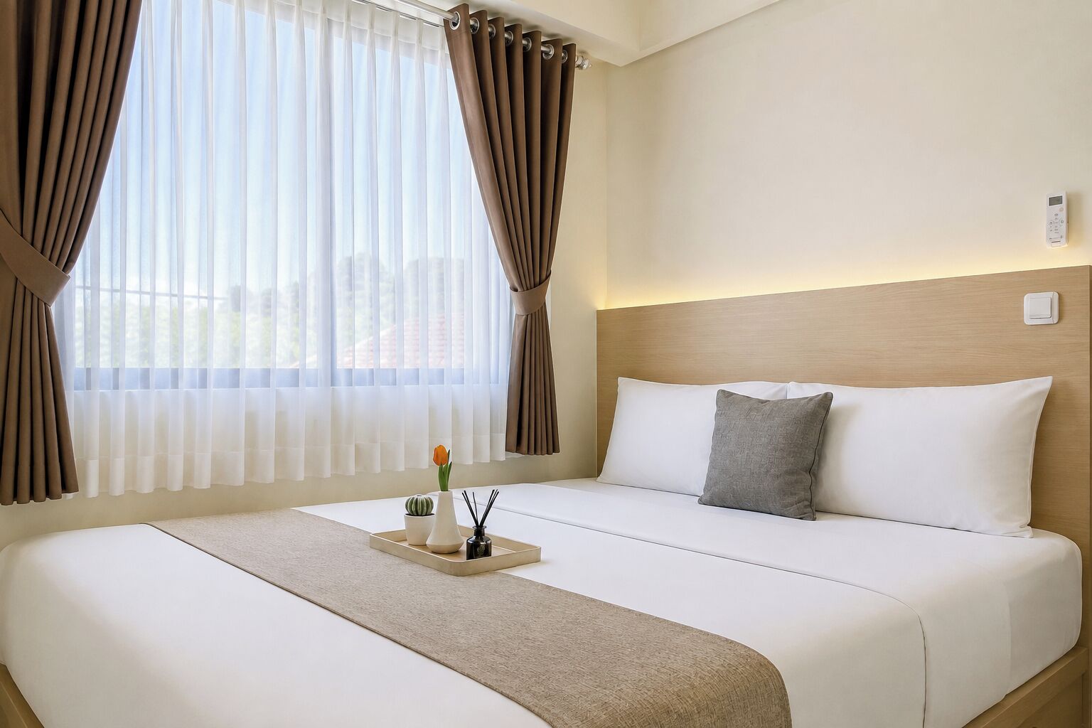 A hotel room with a large bed, a bedside table with a vase and candles, and a window with curtains.