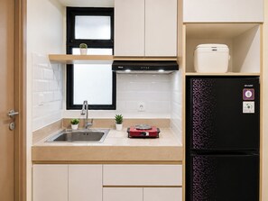 A compact kitchen with a sink, a stove, a refrigerator, and a window with a plant. - Modern Warm 2Br At Apartment Meikarta District 2 (Cikarang)