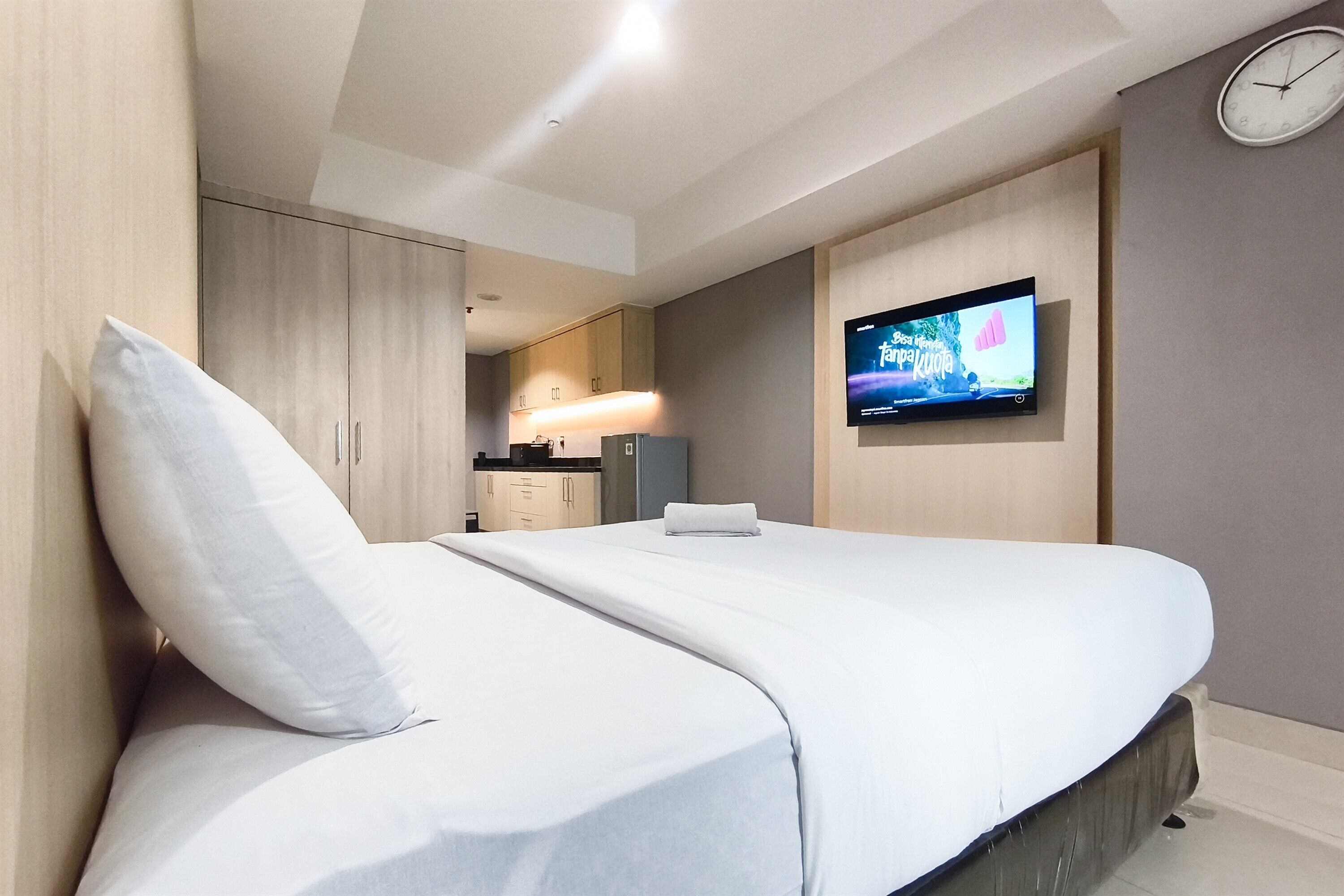 A modern hotel room with a bed, a flat-screen TV mounted on the wall, and a clock on the wall.