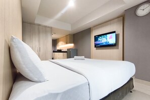 A modern hotel room with a bed, a flat-screen TV mounted on the wall, and a clock on the wall. - Well Appointed Studio At Apartment The Pinncale (Semarang)