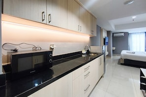 A modern kitchen with a black countertop, stainless steel appliances, and light-colored cabinetry. - Well Appointed Studio At Apartment The Pinncale (Semarang)