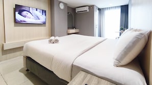 Quarto de hotel com cama, televisão fixada na parede, relógio e ar condicionado.