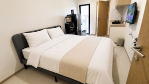 A hotel room with a bed, a television mounted on the wall, and a door leading to the bathroom. - Bright And Homey Studio Room At Apartment Meikarta District 1 (Cikarang)
