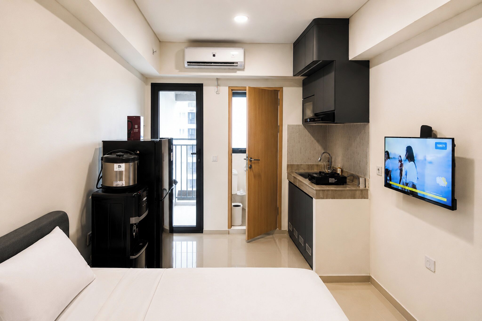 Una habitación de hotel funcional con cama, kitchenette, televisión y vistas al exterior.