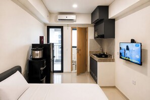 Una habitación de hotel funcional con cama, kitchenette, televisión y vistas al exterior.
