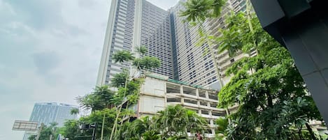 A modern high-rise building with a mix of glass and concrete facades, surrounded by lush greenery and palm trees.