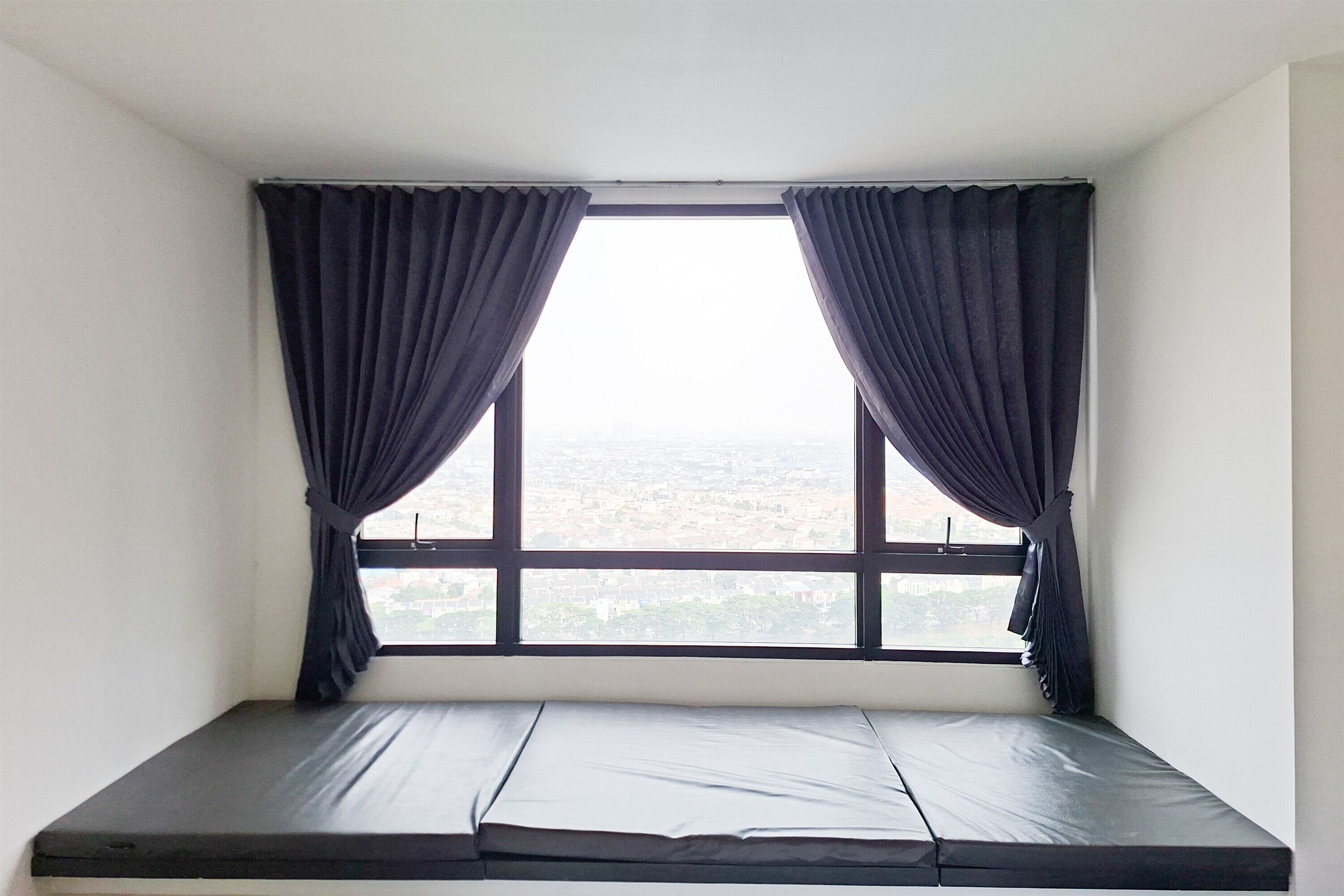 A room with a single window, a mattress, and curtains.