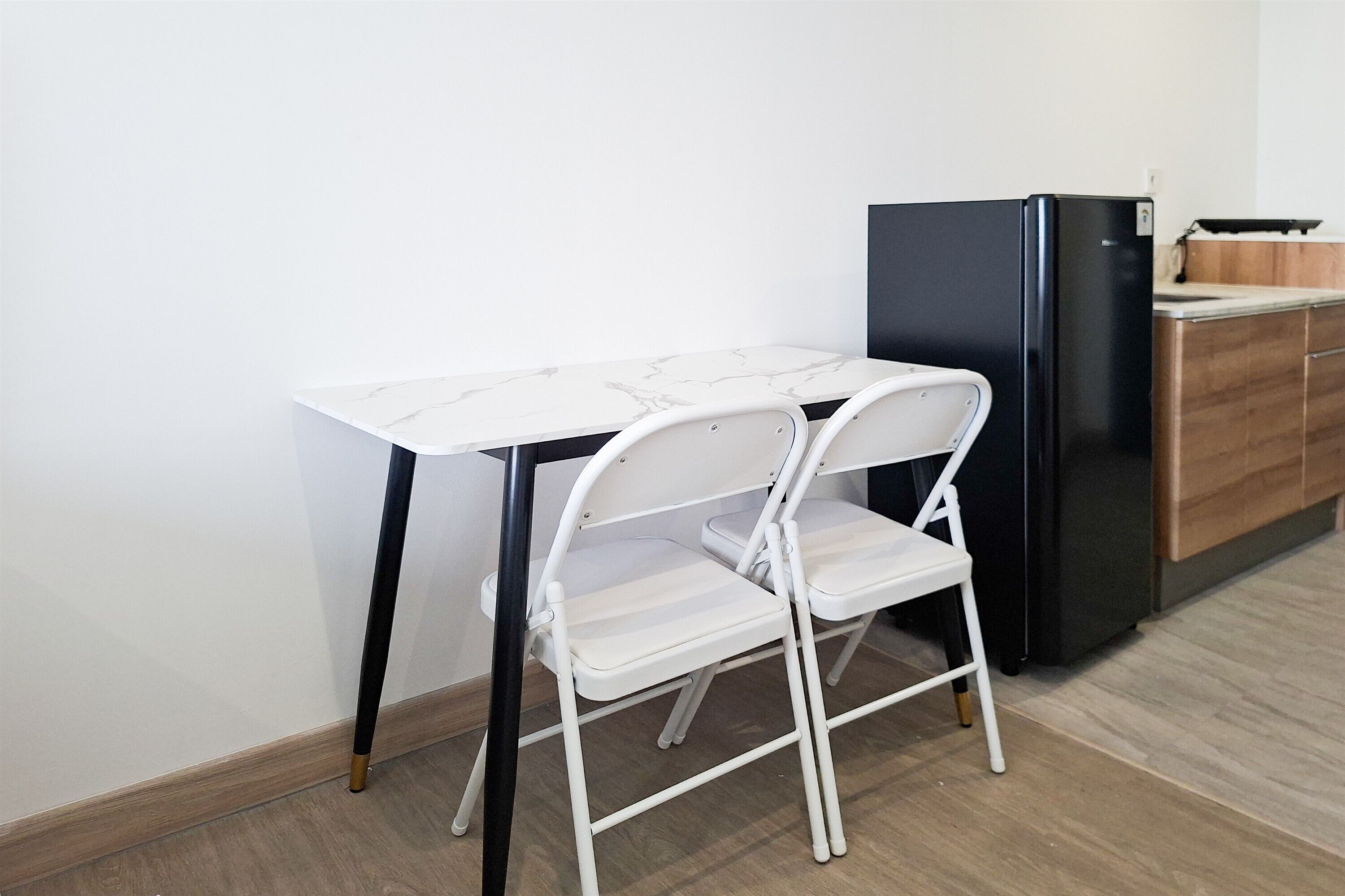 A compact kitchen with a white marble table, a white folding chair, and a black refrigerator.