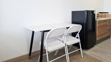A compact kitchen with a white marble table, a white folding chair, and a black refrigerator.