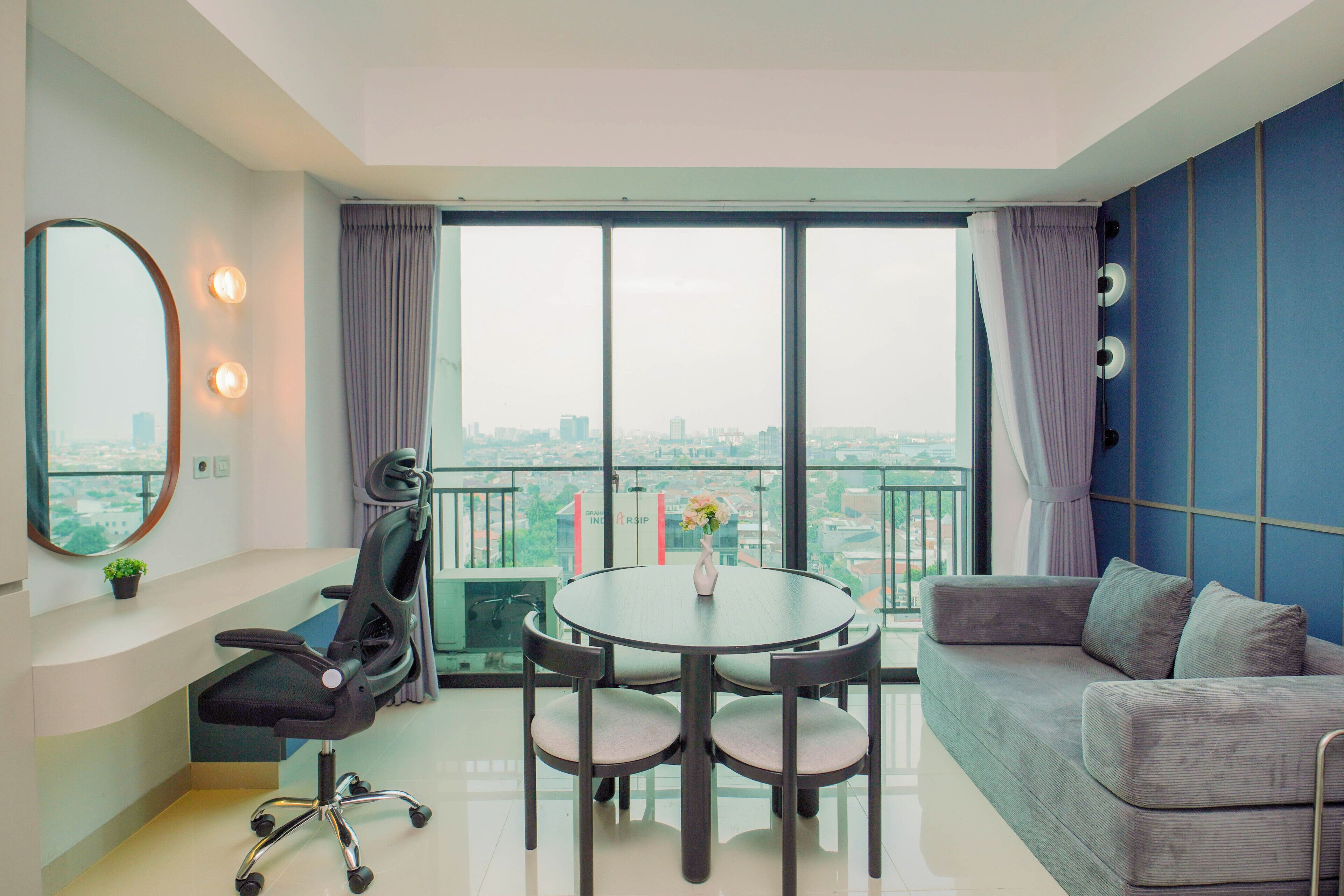 A modern living room with a round table, a sofa, and a chair. There is a large window with a view of a cityscape.