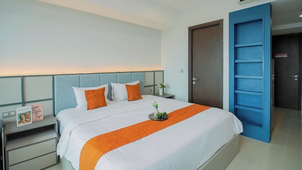 A hotel room with a bed, a nightstand, a bedside table, an air conditioning unit, and a blue door. - Affordable Value Studio At Apartment Nine Residence (Jakarta)