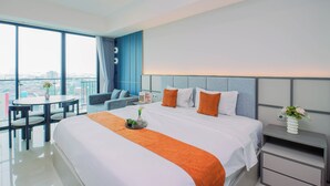 A modern hotel room with a large bed, a small table, a sofa, and a view of the city. - Affordable Value Studio At Apartment Nine Residence (Jakarta)