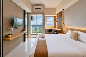 A modern hotel room with a large bed, a TV, a balcony with a city view, and a desk area. - Neat And Tidy Studio At Apartment Parkland Avenue (Tangerang)