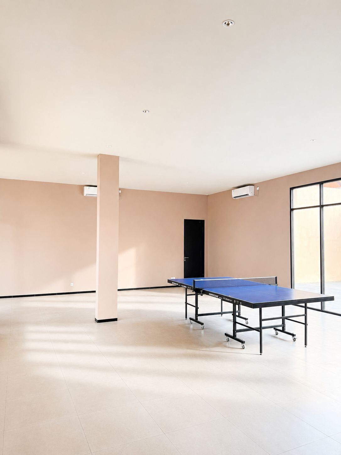 A spacious room with a ping pong table, air conditioning units, and a door.