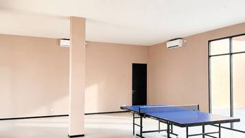 A spacious room with a ping pong table, air conditioning units, and a door.