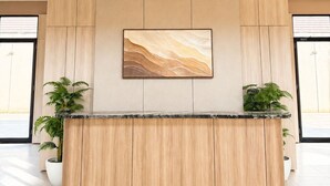 A reception desk with a marble top, flanked by two potted plants, in a modern lobby with a large abstract painting above. - Serene Modern 1BR at Sora Villa Cilegon (Cilegon)
