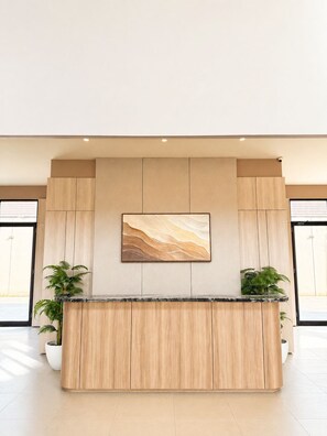 A reception desk with a marble top, flanked by two potted plants, in a modern lobby with a large abstract painting above. - Serene Modern 1BR at Sora Villa Cilegon (Cilegon)