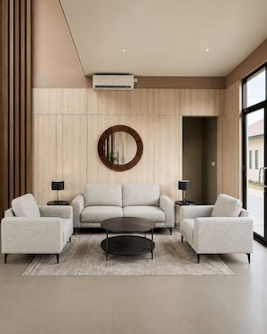A modern living room with a sofa, two armchairs, a coffee table, and a round mirror on the wall. - Serene Modern 1BR at Sora Villa Cilegon (Cilegon)
