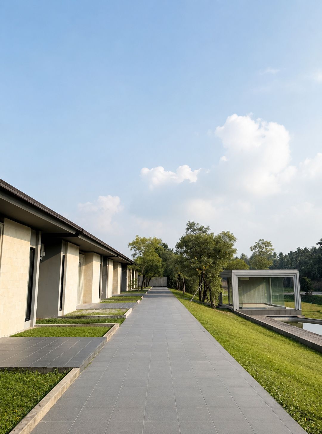 A pathway leading to a modern building with a flat roof and large windows, surrounded by greenery and a clear sky.