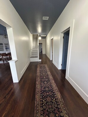A hallway with a patterned rug, white walls, and a dark ceiling.
