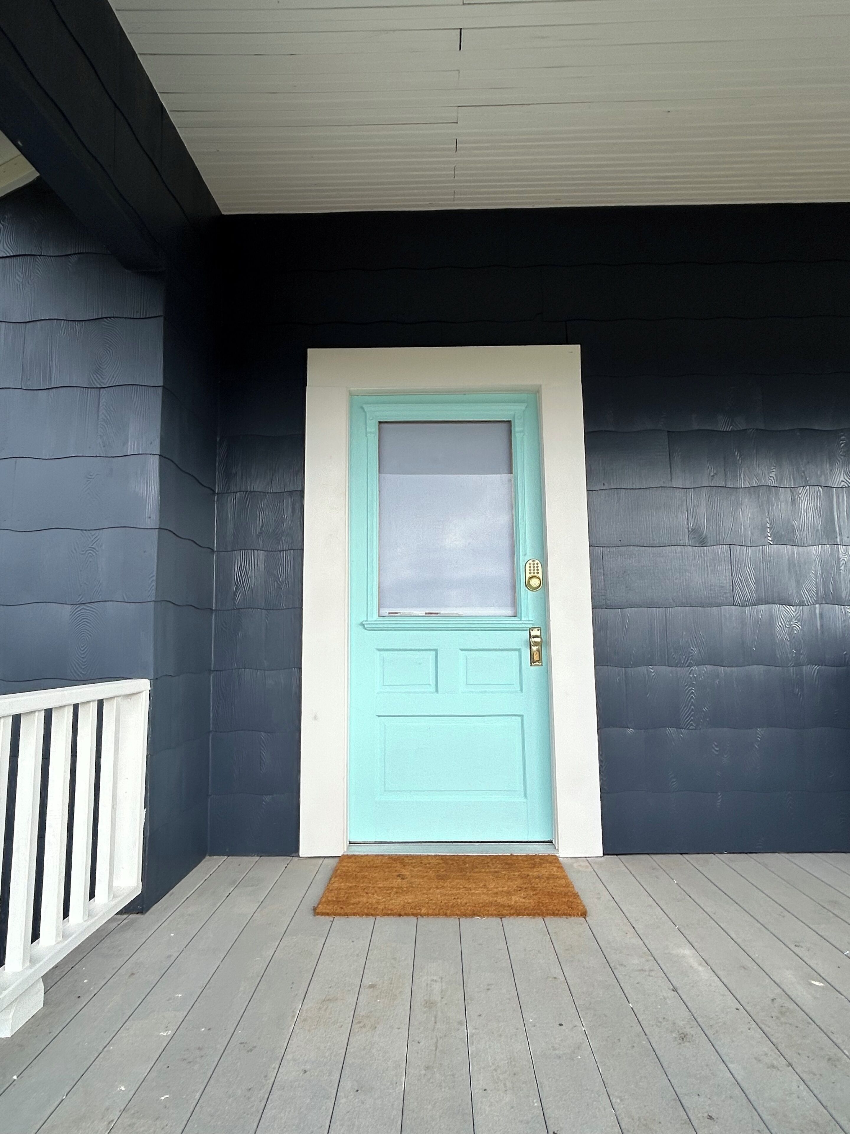 A front door with a window, a doormat, and a white railing.