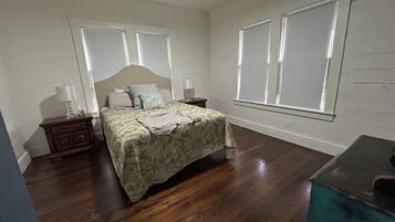 A bedroom with a bed, nightstands, a dresser, and large windows.