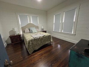 A bedroom with a bed, nightstands, a dresser, and large windows.