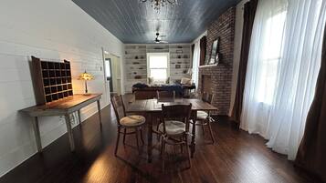 A dining area with a wooden table and chairs, a chandelier, and a brick fireplace.