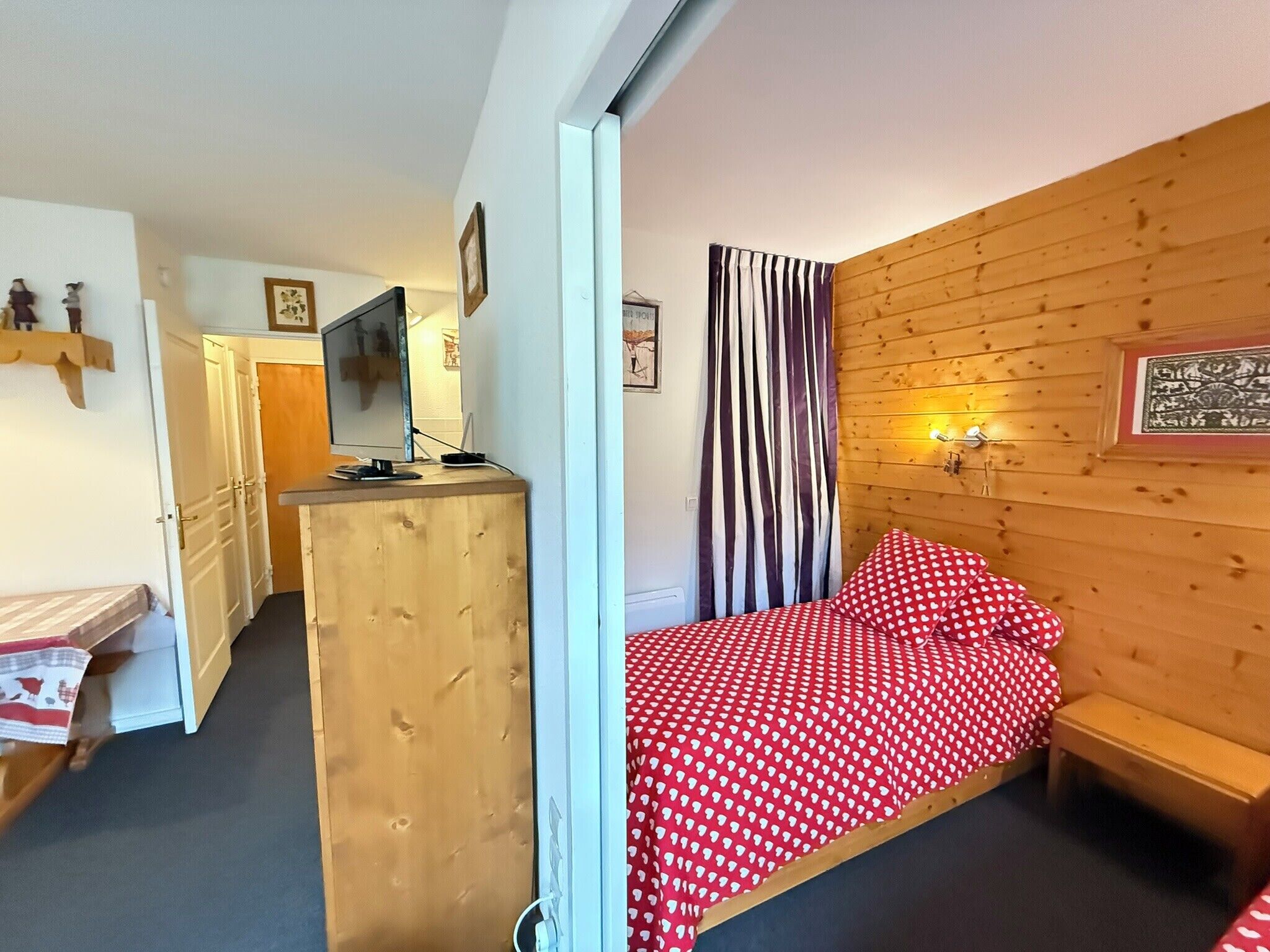 A bedroom with a bed, a wooden headboard, a television, and a desk with a computer.