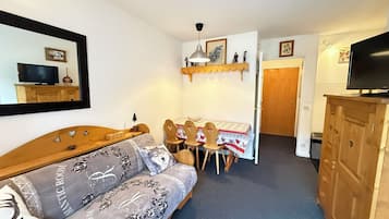 Une pièce de taille modeste comprenant un lit, une petite table avec des chaises, un téléviseur et un meuble.