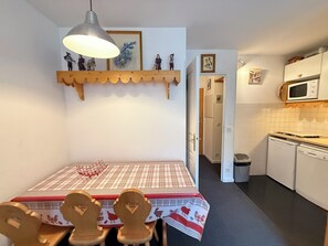 A compact kitchen with a dining area, featuring a table with a plaid tablecloth, a hanging light fixture, and a microwave above the counter.