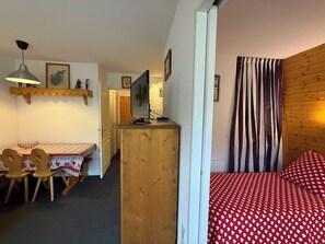 A compact room with a bed, a desk with a computer, a dining area, and a wooden partition. - Appart 4 pers • proche pistes• Piscine et sauna • Risoul (Risoul)