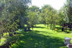 A grassy outdoor area with a swing set, seating, and trees.