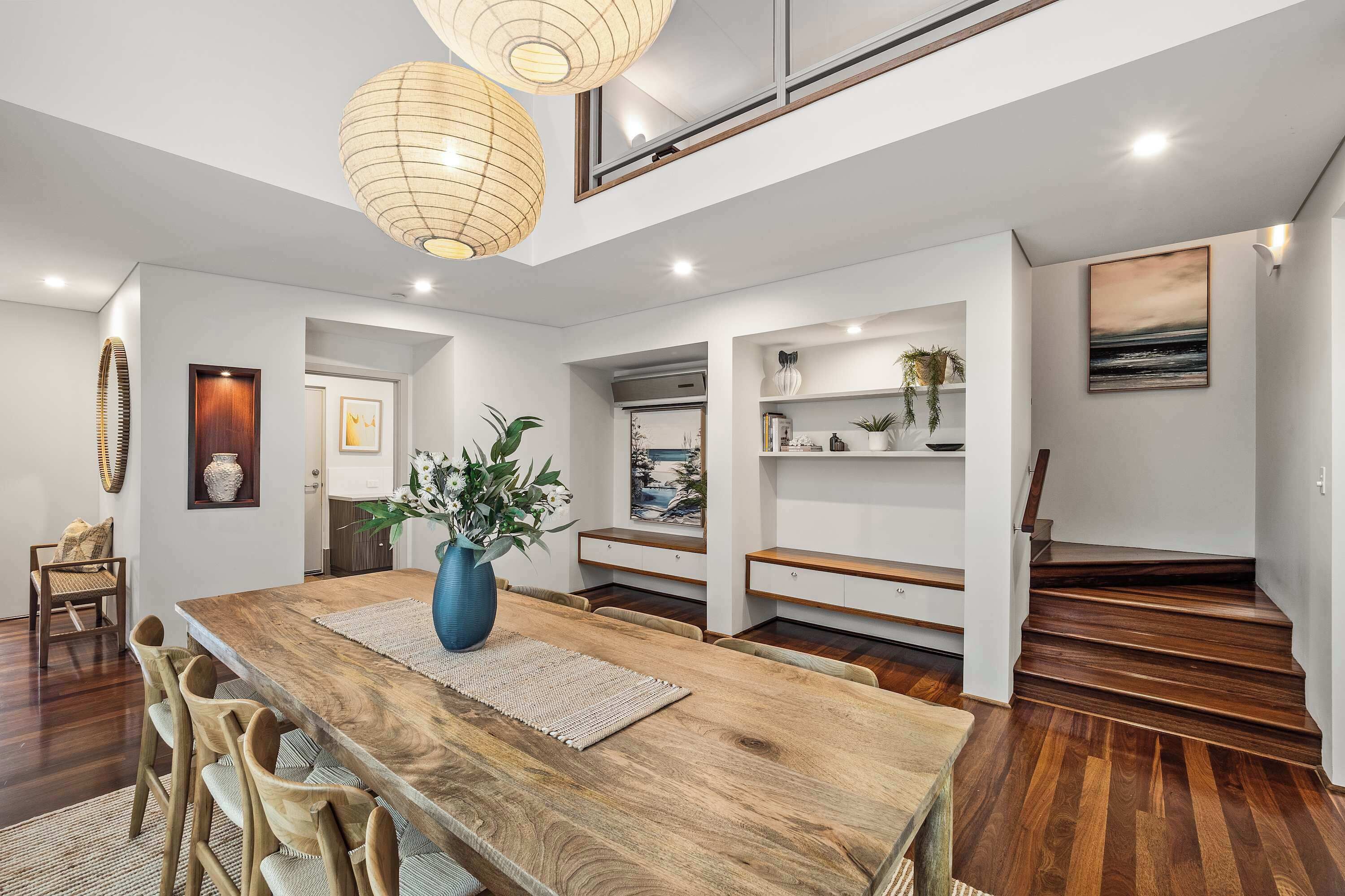 A modern interior with a wooden dining table, chairs, a vase of flowers, and a staircase.