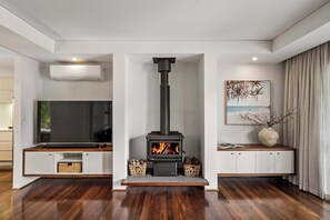 A modern living room with a wood-burning stove, a flat-screen TV, and a painting on the wall. - Coastal Rhythms - A Sophisticated Seaside Retreat (Dunsborough)