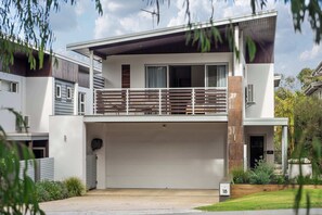 Een modern huis met twee verdiepingen, een plat dak, een balkon met houten spijlen en een garage.