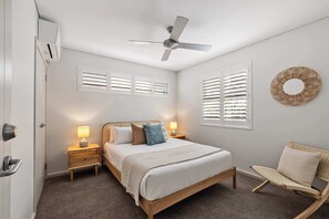 A bedroom with a bed, bedside lamps, a ceiling fan, and a window with shutters. - Coastal Rhythms - A Sophisticated Seaside Retreat (Dunsborough)