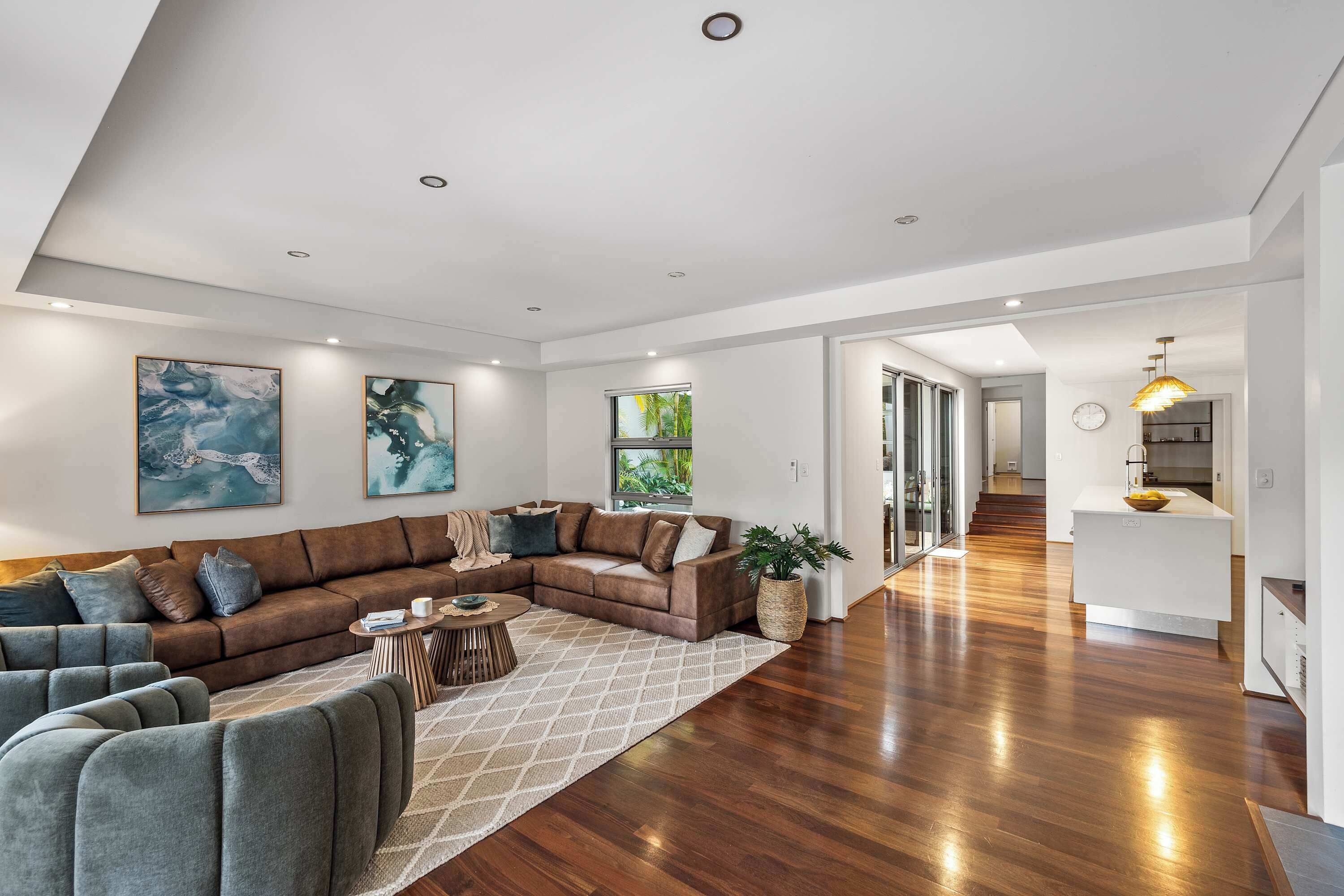 A modern living room with a sectional sofa, a coffee table, and a rug. There is a kitchen area visible in the background.