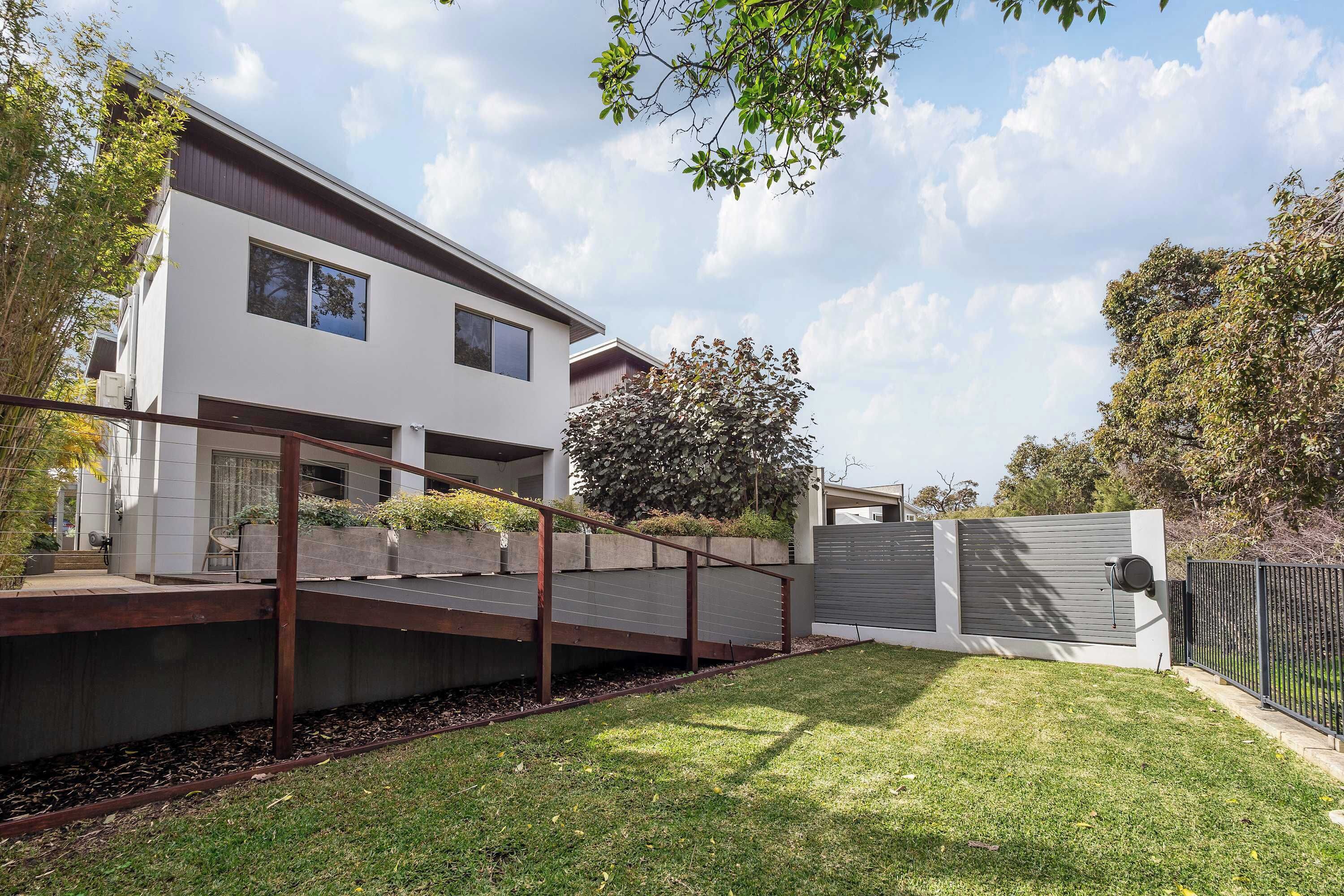 A modern two-story residential building with a flat roof, large windows, and a covered outdoor area with a wooden deck.