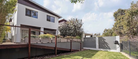 Un edificio residenziale moderno, su due piani, con tetto piatto, ampie finestre e una zona esterna coperta con un patio in legno.