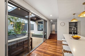 A modern kitchen with a wooden countertop, a bowl of fruit, and a dining area with white chairs. - Coastal Rhythms - A Sophisticated Seaside Retreat (Dunsborough)