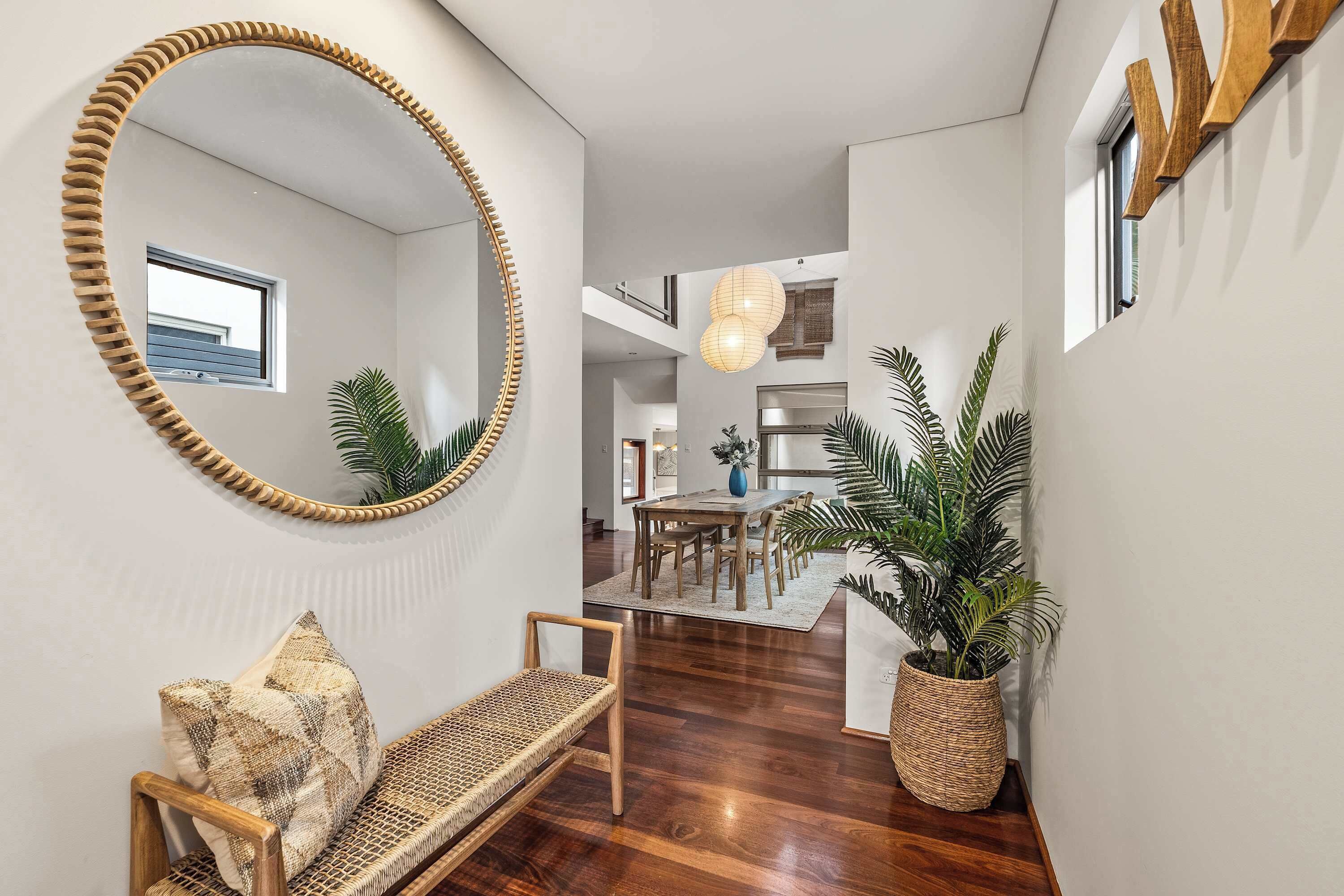 A hallway with a wooden bench, a large mirror, and a potted plant.