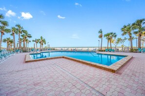 A rectangular swimming pool with a tiled deck, surrounded by palm trees and lounge chairs. - 🌞CBC 1-15A – Water views from every window! 5 balconies, heated pool, pickleball, gym. (Clearwater Beach)