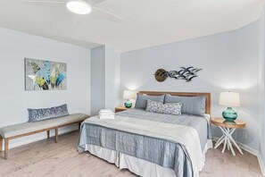 A bedroom with a bed, bedside tables, a bench, and wall art. - 🌞CBC 1-15A – Water views from every window! 5 balconies, heated pool, pickleball, gym. (Clearwater Beach)