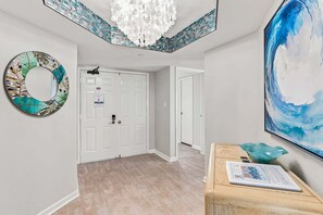 A hallway with a white door, a chandelier, a mosaic wall, and a painting. - 🌞CBC 1-15A – Water views from every window! 5 balconies, heated pool, pickleball, gym. (Clearwater Beach)