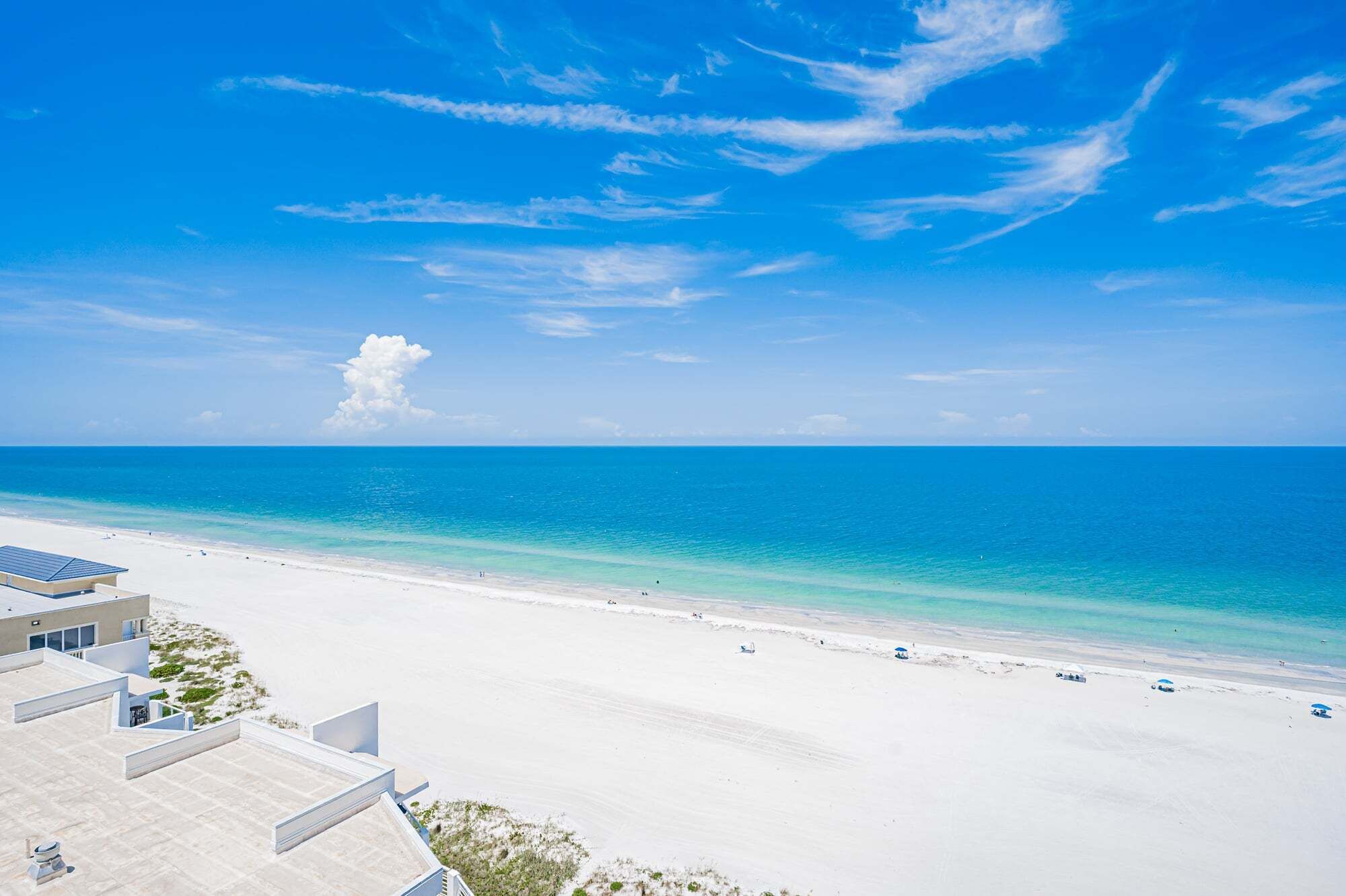 A beach view with a clear sky, a sandy shore, and a modern building with a flat roof.