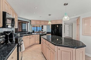 Cocina moderna con una isla grande, encimeras negras y armarios de madera clara.